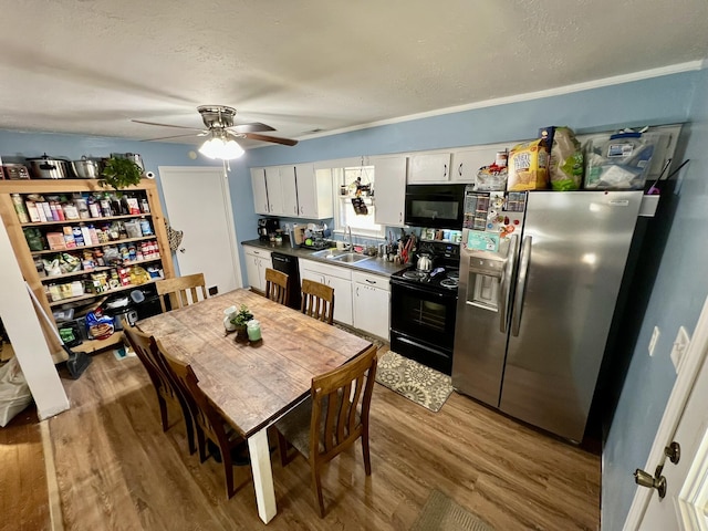 kitchen with black appliances, a sink, dark countertops, wood finished floors, and white cabinets