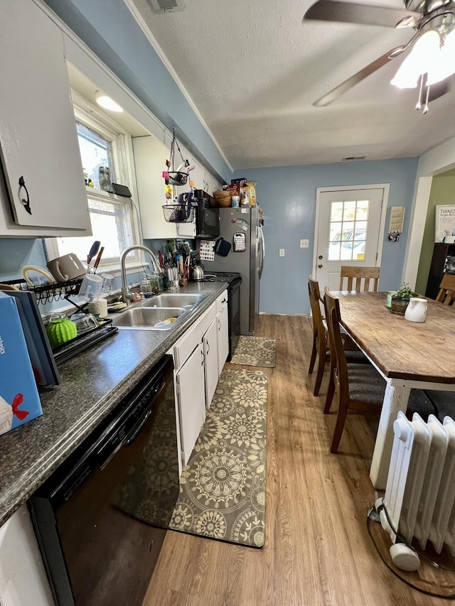 kitchen featuring light wood-type flooring, black appliances, a sink, plenty of natural light, and dark countertops