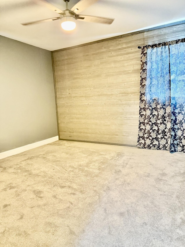 carpeted empty room with wood walls and a ceiling fan