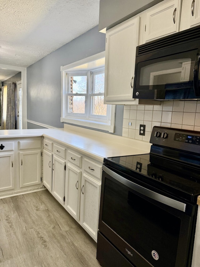 kitchen with white cabinets, light countertops, a textured ceiling, light wood-type flooring, and black appliances