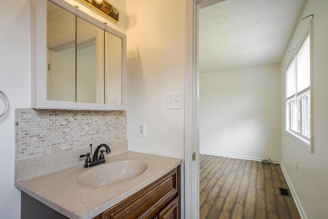 bathroom featuring vanity, wood finished floors, visible vents, baseboards, and backsplash