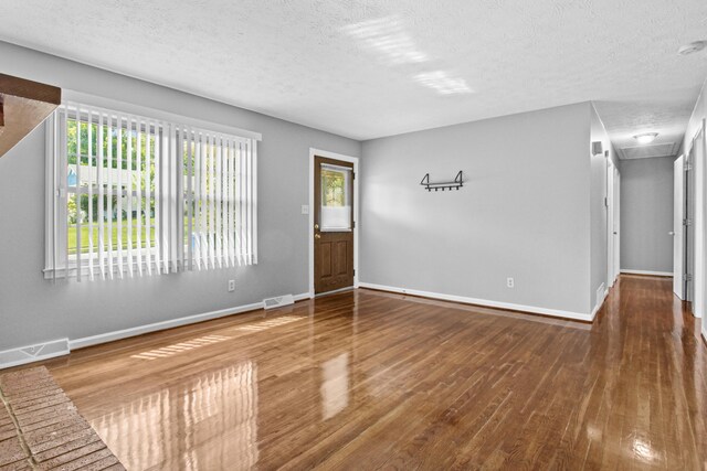 empty room with baseboards, wood finished floors, visible vents, and a textured ceiling