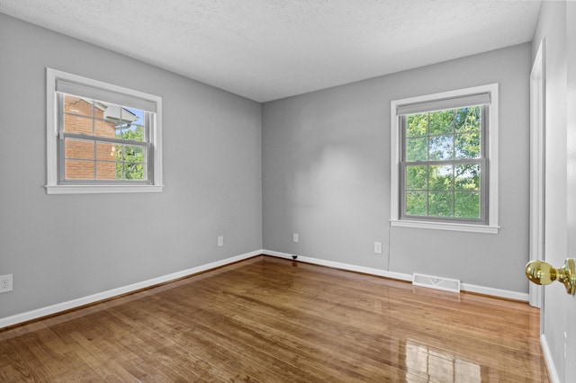 empty room with a textured ceiling, wood finished floors, visible vents, and baseboards