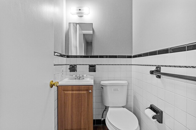 bathroom featuring vanity, tile walls, toilet, and a wainscoted wall