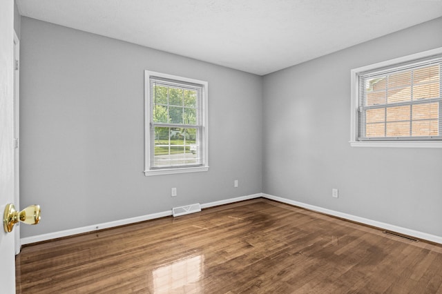 empty room featuring dark wood finished floors, visible vents, and baseboards