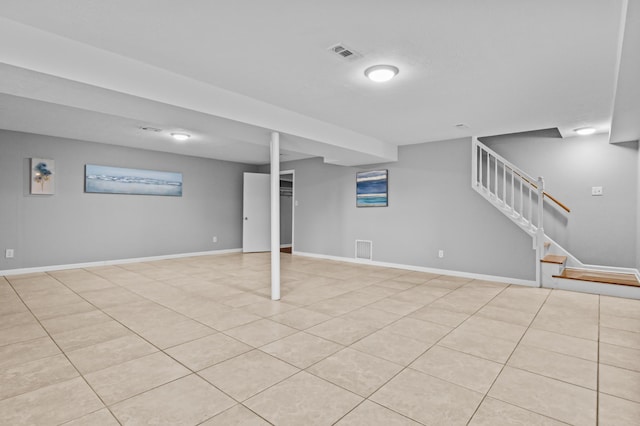 finished basement featuring visible vents, baseboards, light tile patterned flooring, and stairs