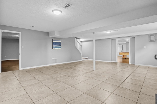 finished below grade area featuring stairs, light tile patterned flooring, and visible vents