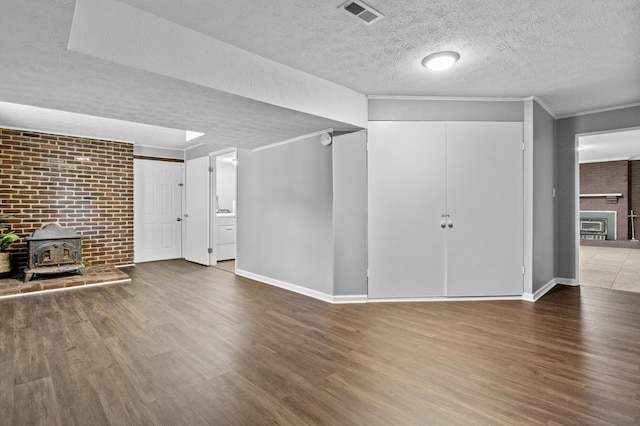 below grade area with visible vents, a textured ceiling, wood finished floors, crown molding, and a wood stove