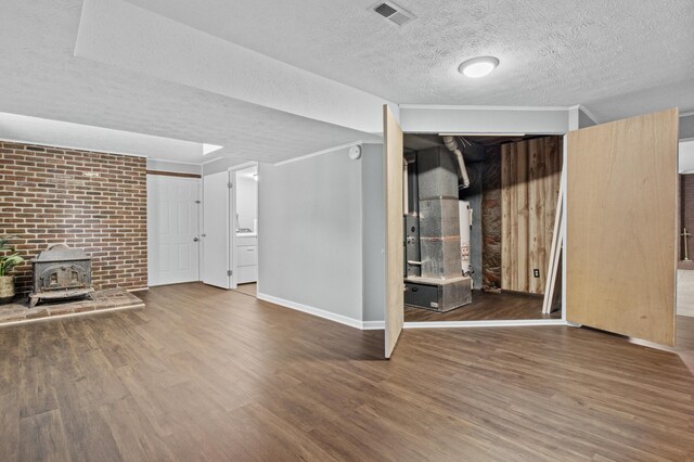 unfurnished living room with a wood stove, wood finished floors, visible vents, and a textured ceiling