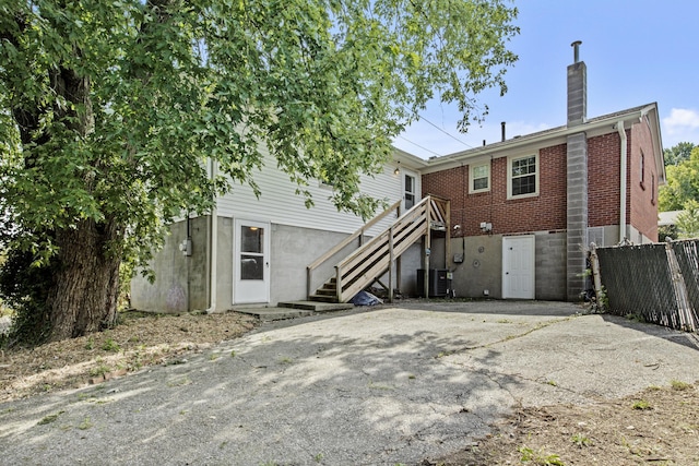 back of property featuring brick siding, a chimney, stairs, and fence