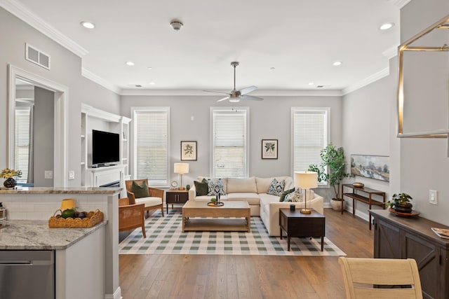 living area with light wood-style flooring, a ceiling fan, visible vents, and ornamental molding