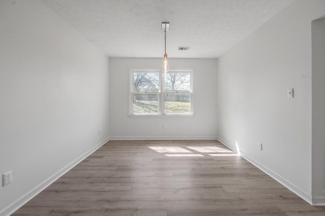 unfurnished dining area featuring baseboards, wood finished floors, visible vents, and a textured ceiling