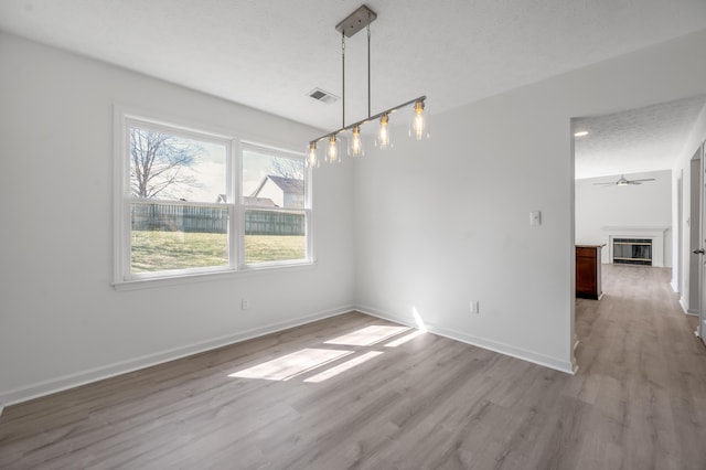 spare room featuring a ceiling fan, wood finished floors, visible vents, baseboards, and a glass covered fireplace