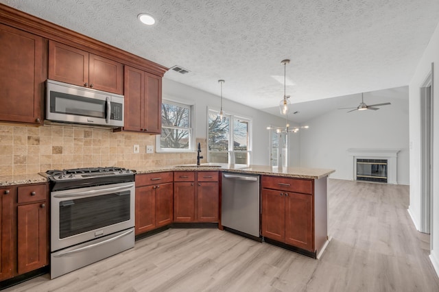 kitchen with a sink, light wood-style flooring, appliances with stainless steel finishes, and a peninsula