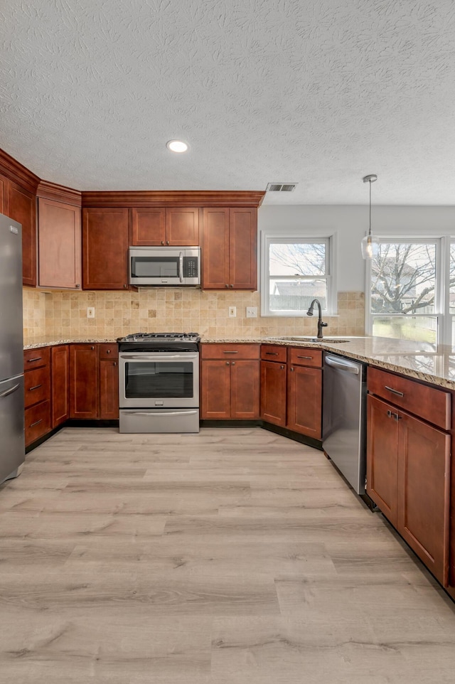 kitchen with visible vents, light stone counters, light wood-style floors, appliances with stainless steel finishes, and decorative backsplash