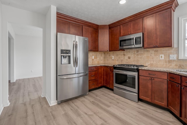 kitchen featuring light wood-type flooring, stainless steel appliances, light stone countertops, and tasteful backsplash