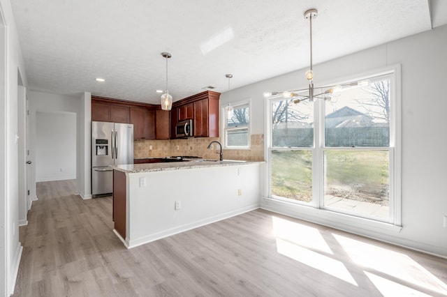 kitchen with a peninsula, light wood-style flooring, light stone countertops, and stainless steel appliances