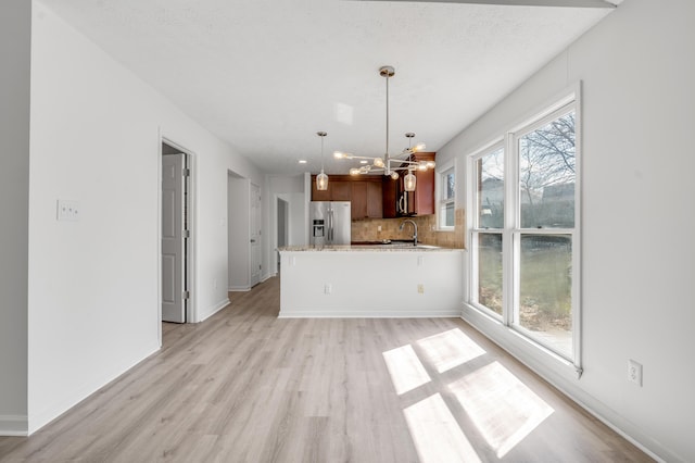 kitchen with light wood-style flooring, decorative light fixtures, stainless steel fridge, a peninsula, and decorative backsplash