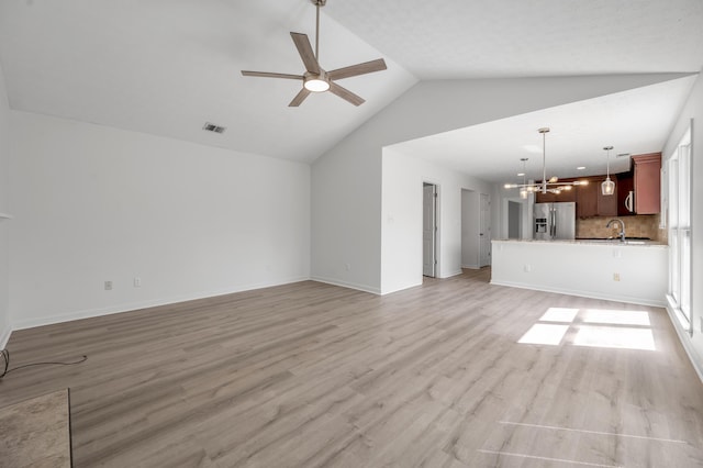 unfurnished living room with visible vents, vaulted ceiling, ceiling fan with notable chandelier, light wood-style floors, and a sink