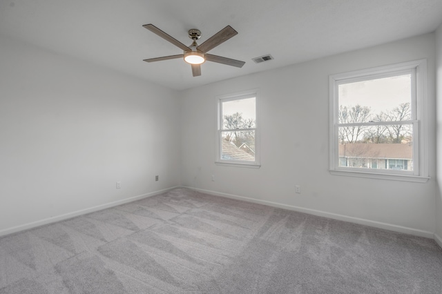 empty room featuring visible vents, plenty of natural light, carpet flooring, and ceiling fan