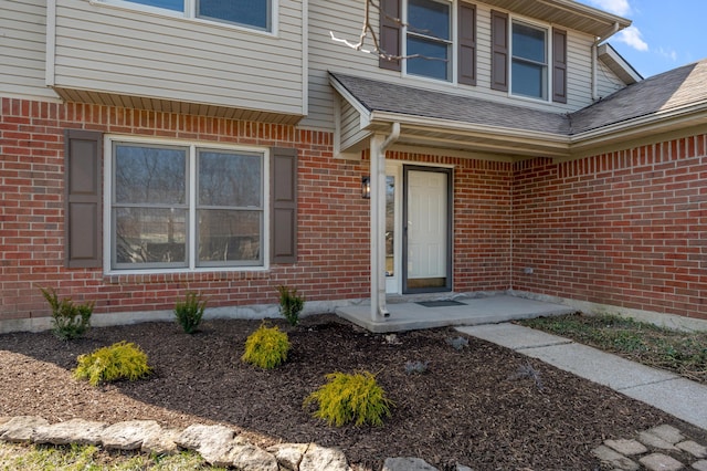 view of exterior entry with brick siding and a shingled roof