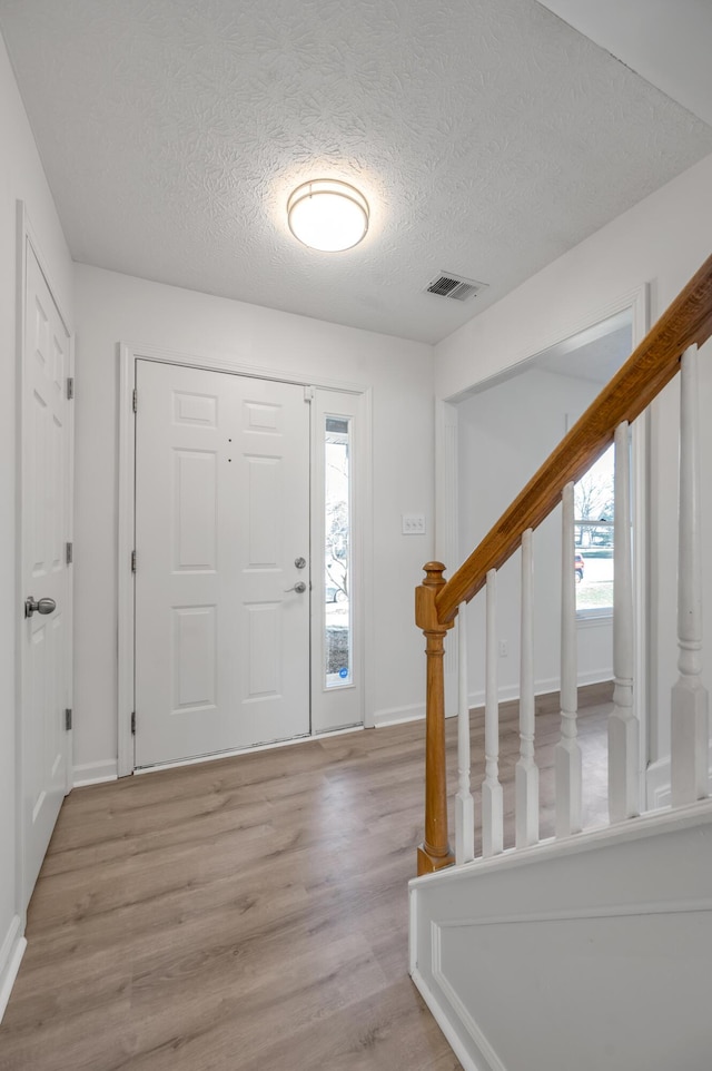 entrance foyer with stairway, baseboards, visible vents, a textured ceiling, and light wood-type flooring