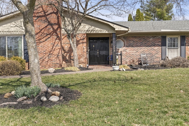 view of exterior entry with brick siding, a lawn, and a shingled roof