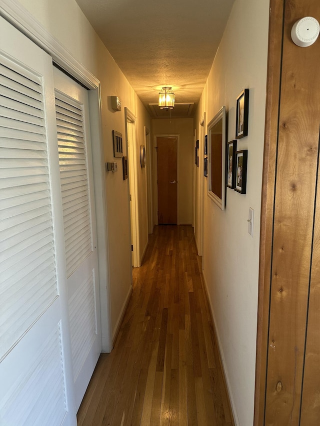 hallway featuring dark wood finished floors, a textured ceiling, attic access, and baseboards