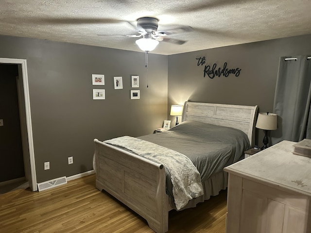 bedroom with visible vents, baseboards, a textured ceiling, and light wood finished floors