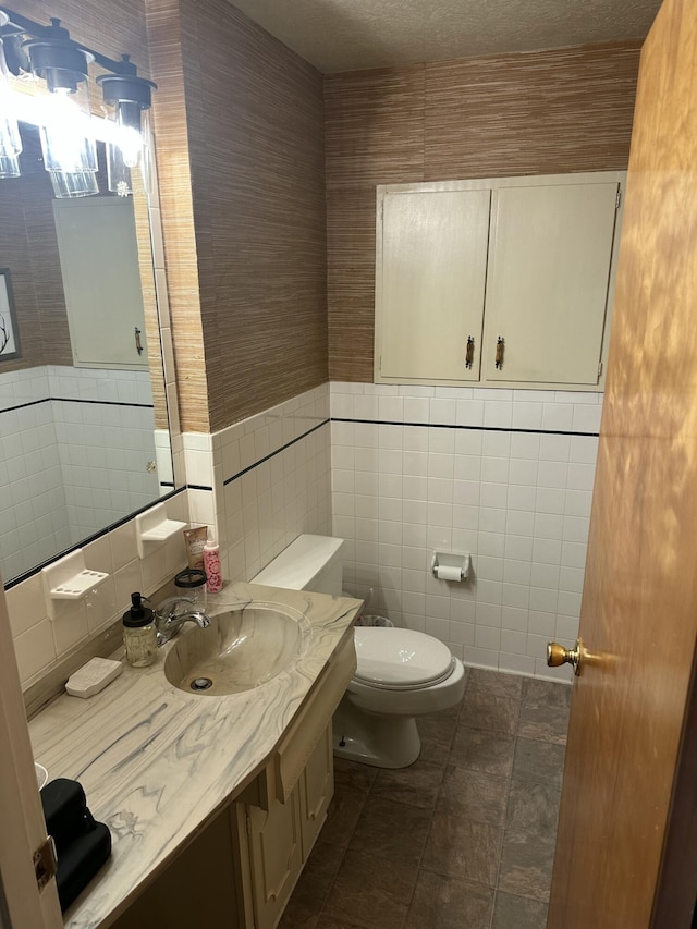 half bathroom with tile patterned floors, vanity, toilet, and tile walls