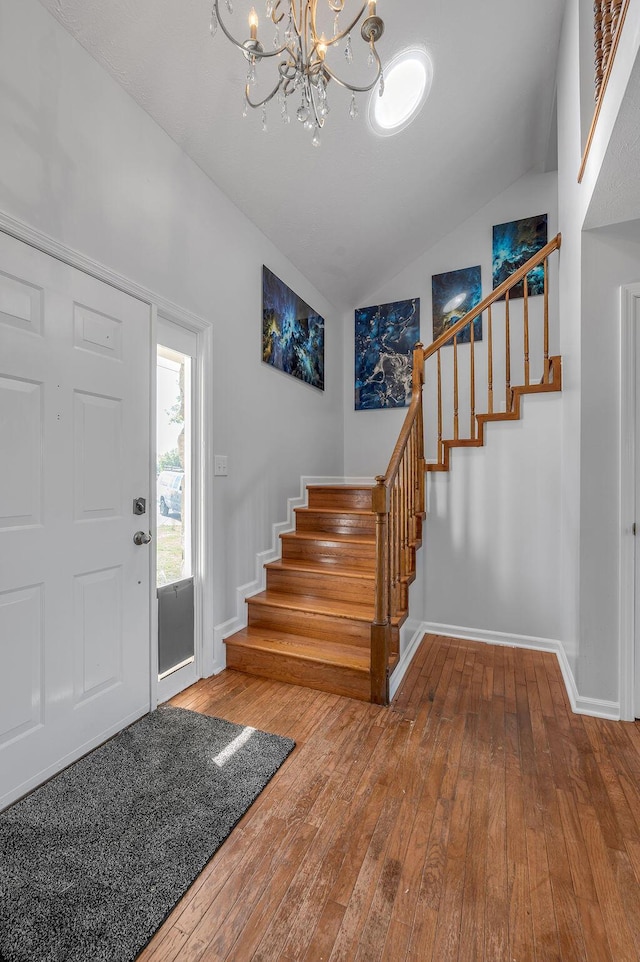 foyer entrance with a notable chandelier, hardwood / wood-style floors, baseboards, stairs, and vaulted ceiling