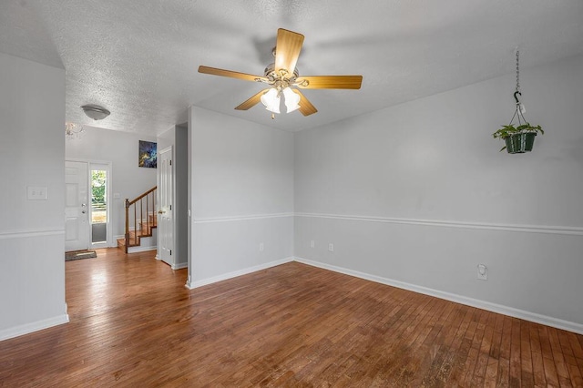 unfurnished room featuring stairway, a textured ceiling, baseboards, and hardwood / wood-style flooring