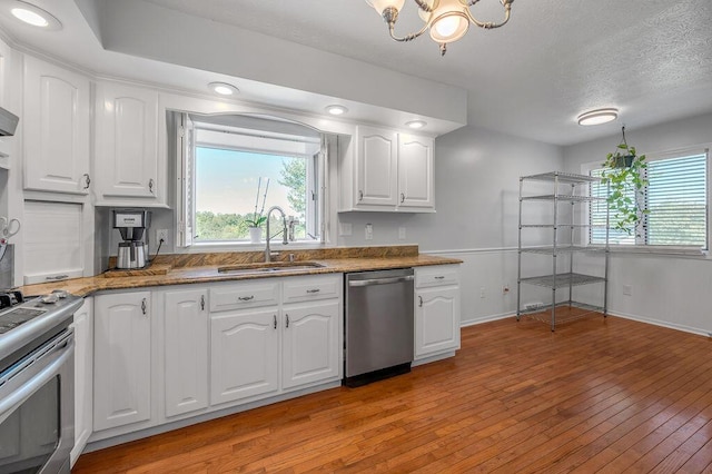 kitchen featuring light wood-type flooring, a wealth of natural light, white cabinets, stainless steel appliances, and a sink