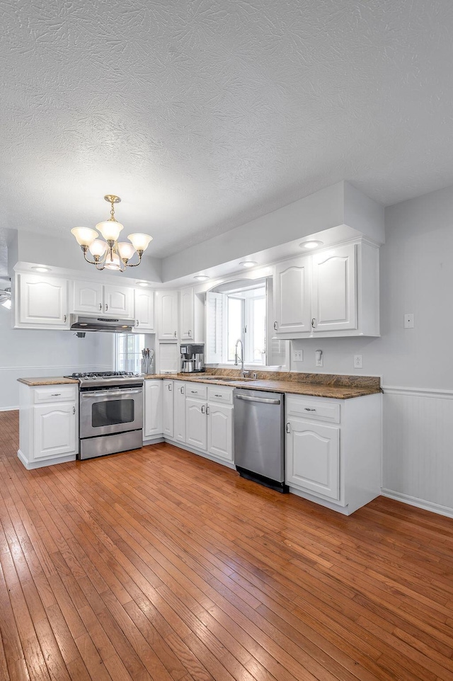 kitchen featuring light wood-type flooring, a notable chandelier, appliances with stainless steel finishes, and white cabinets