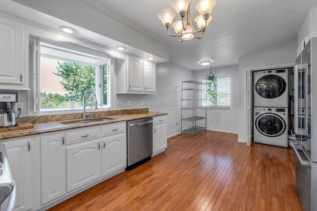 kitchen with stacked washer / dryer, light wood-type flooring, stainless steel dishwasher, white cabinetry, and a sink