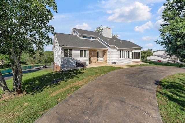 view of front facade featuring a chimney, a shingled roof, a front yard, and fence