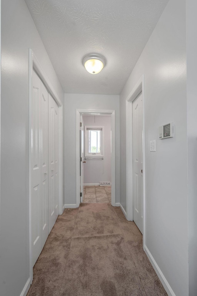 hall featuring light colored carpet, a textured ceiling, and baseboards