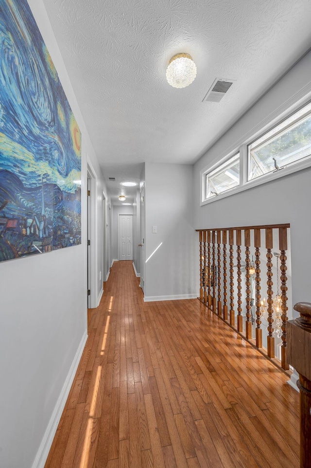 hallway with hardwood / wood-style floors, baseboards, visible vents, and a textured ceiling