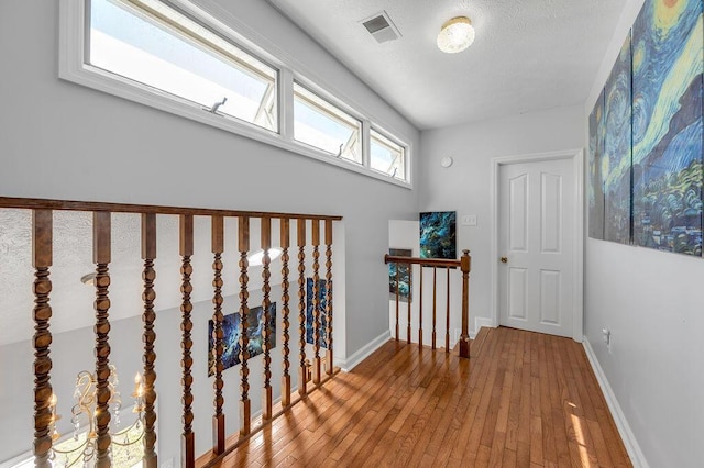 hallway with hardwood / wood-style flooring, an upstairs landing, baseboards, and visible vents