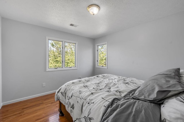 bedroom featuring visible vents, a textured ceiling, baseboards, and wood finished floors