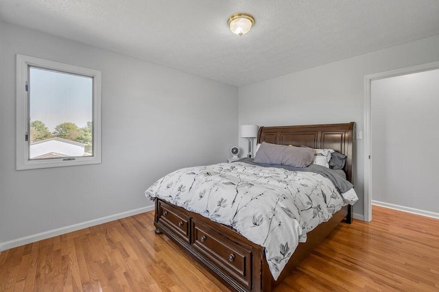 bedroom featuring baseboards, a textured ceiling, and light wood-style flooring