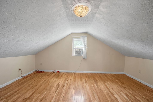 bonus room featuring cooling unit, baseboards, hardwood / wood-style flooring, vaulted ceiling, and a textured ceiling