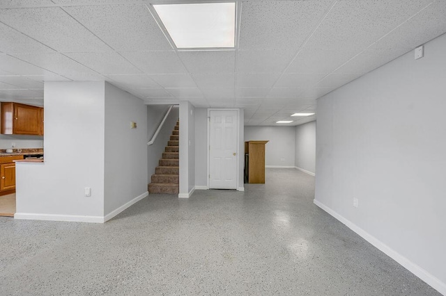 finished basement with a drop ceiling, stairs, and baseboards