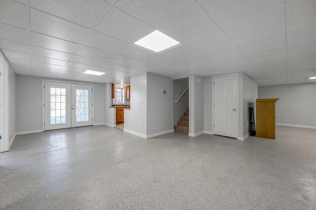 basement with stairway, a paneled ceiling, baseboards, and french doors