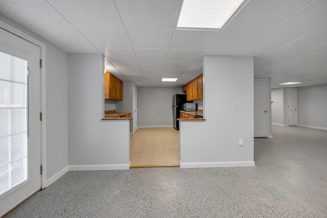 kitchen with baseboards, a paneled ceiling, brown cabinets, and freestanding refrigerator