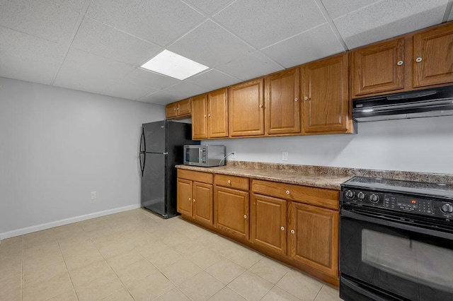 kitchen with black appliances, brown cabinetry, under cabinet range hood, and a paneled ceiling