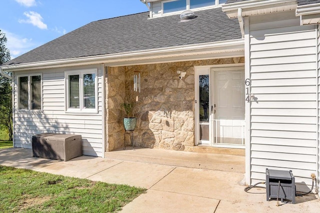 exterior space featuring a patio area, stone siding, and a shingled roof