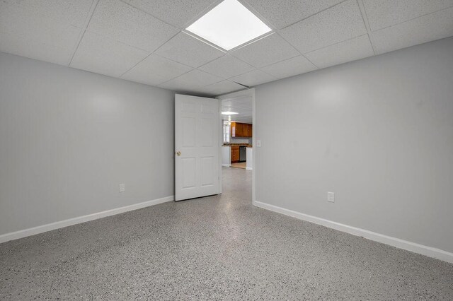 spare room with a drop ceiling, speckled floor, and baseboards