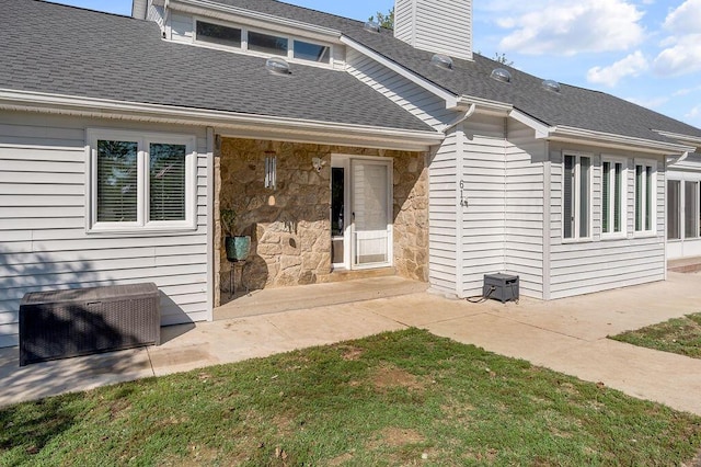 rear view of house with stone siding, a patio, a chimney, and a shingled roof