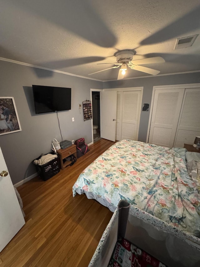 bedroom with visible vents, two closets, wood finished floors, and a textured ceiling